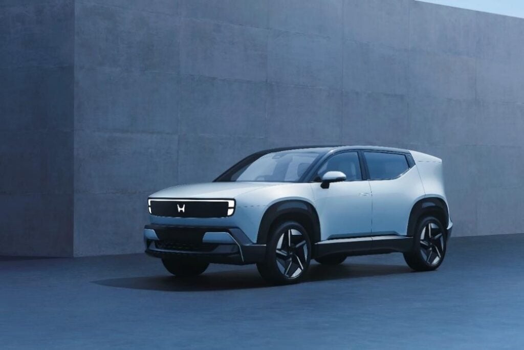 Front three-quarter view of the new Honda 0 α (Alpha) electric SUV concept in light silver, showcasing its futuristic illuminated 'H' logo light bar, unveiled at the Japan Mobility Show 2025.