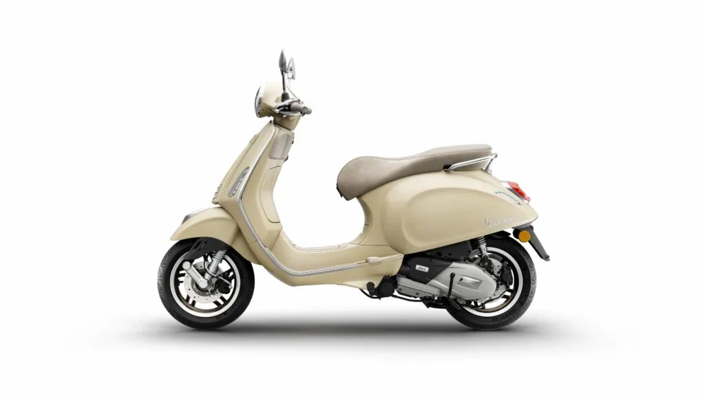 New Vespa Primavera or Sprint S scooter in a light beige or sand color, showcasing the updated design, new 12-inch wheels, and a refined seat.
