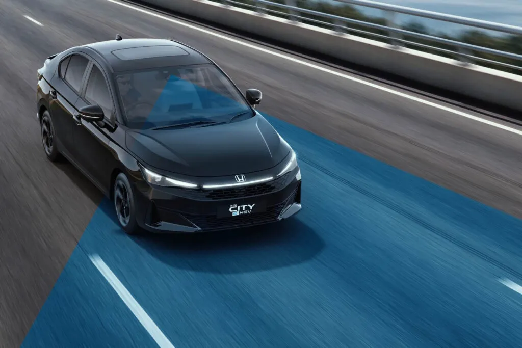 Black Honda City e:HEV driving on a road with a blue beam illustrating its driver-assist sensor technology