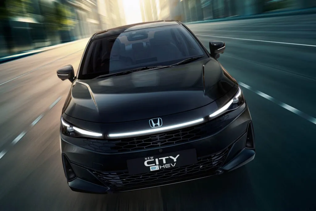 Front view of a black Honda City e:HEV driving on a city street with a glowing LED light bar
